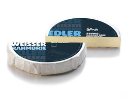 KI generiert: Das Bild zeigt ein Stück weißen Käse, das auf einer schwarzen Schieferplatte in vier Portionen geschnitten ist, daneben ist eine verpackte, identische Käserolle abgebildet.