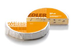 KI generiert: Das Bild zeigt ein Stück weißen Käse, das auf einer schwarzen Schieferplatte in vier Portionen geschnitten ist, daneben ist eine verpackte, identische Käserolle abgebildet.