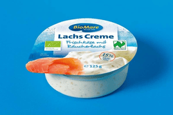 KI generiert: Auf dem Bild befindet sich eine durchsichtige Plastikverpackung mit Ziegenfrischkäse, der mit Kräutern und rosa Pfefferkörnern verfeinert ist. Das Etikett trägt die Aufschrift "ZiegenFRISCHKÄSE" der Marke Biovela.