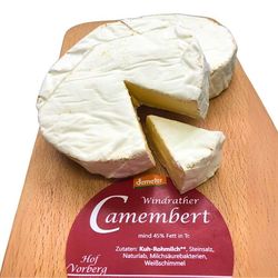 KI generiert: Das Bild zeigt ein Stück weißen Käse, das auf einer schwarzen Schieferplatte in vier Portionen geschnitten ist, daneben ist eine verpackte, identische Käserolle abgebildet.