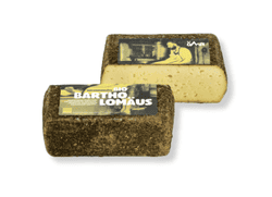 KI generiert: Das Bild zeigt ein Stück weißen Käse, das auf einer schwarzen Schieferplatte in vier Portionen geschnitten ist, daneben ist eine verpackte, identische Käserolle abgebildet.