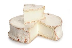 KI generiert: Das Bild zeigt ein Stück weißen Käse, das auf einer schwarzen Schieferplatte in vier Portionen geschnitten ist, daneben ist eine verpackte, identische Käserolle abgebildet.