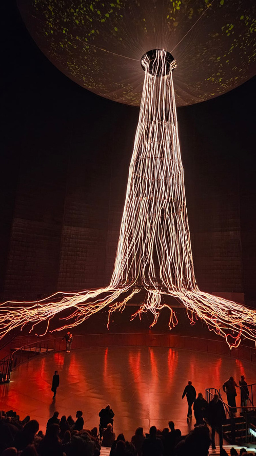 KI generiert: Lichtinstallation in einem großen, dunklen Raum mit Besuchern, die das Kunstwerk betrachten.