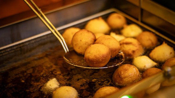 KI generiert: Krapfen werden in heißem Öl frittiert. Ein Sieblöffel hebt sie aus dem Öl.