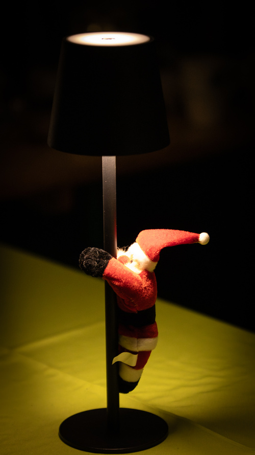 KI generiert: Ein Plüsch-Weihnachtsmann hängt an einer schwarzen Lampe.
