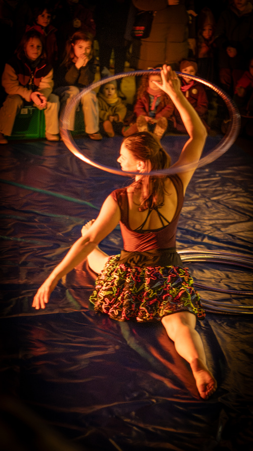 KI generiert: Eine Artistin zeigt eine Hula-Hoop-Performance für zuschauende Kinder.