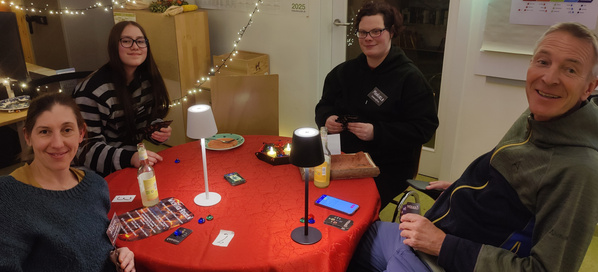 KI generiert: Eine Gruppe von vier Personen spielt ein Kartenspiel an einem Tisch mit roter Tischdecke.