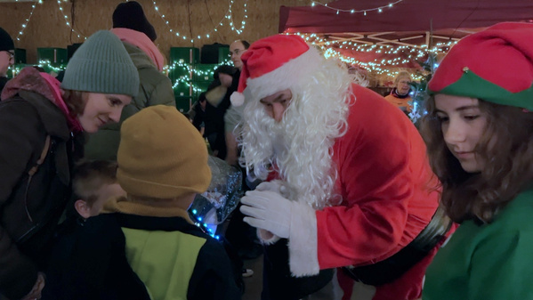 KI generiert: Ein als Weihnachtsmann verkleideter Mann spricht mit Kindern auf einem festlich beleuchteten Markt.