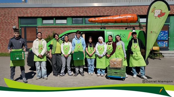 KI generiert: Eine Gruppe junger Menschen steht vor einem Fahrzeug mit einer großen Karotte auf dem Dach. Text: "© Daniel Niemann".