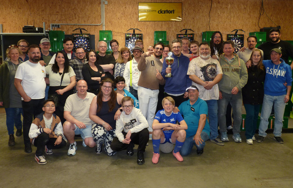 KI generiert: Eine Gruppe von Menschen posiert mit einem Pokal vor Dartboards.