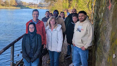 KI generiert: Eine Gruppe von Menschen steht auf einem Uferweg neben einem Fluss.