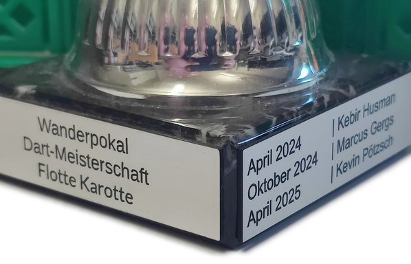 KI generiert: Ein silberner Pokal mit Inschrift: "Wanderpokal Dart-Meisterschaft Flotte Karotte", Namen und Daten auf Plaketten.