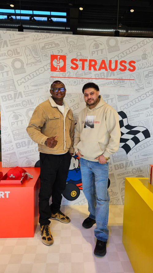 KI generiert: Zwei Männer stehen vor einer Wand mit "STRAUSS"-Logo und Rennmotiven.