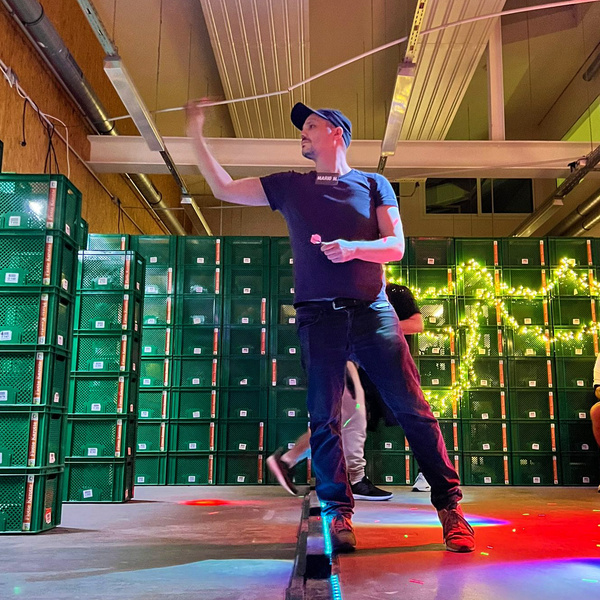 KI generiert: Eine Person in entspannter Pose auf einer Bühne, umgeben von grünen Kisten und Lichterketten.