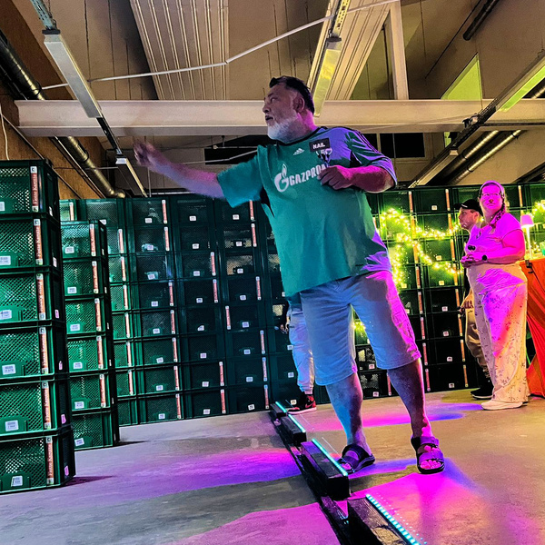 KI generiert: Ein Mann in grüner Kleidung gestikuliert in einem Lager mit gestapelten grünen Kisten.