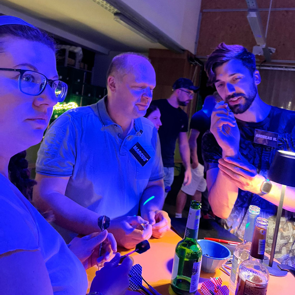 KI generiert: Menschen an einem Tisch beleuchtet in blauem Licht, bei einer Veranstaltung, mit Getränken und Namensschildern.