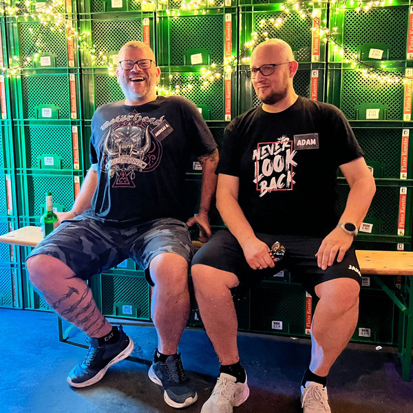 KI generiert: Zwei Männer sitzen vor grünen Kisten. Einer trägt ein Shirt mit der Aufschrift: "NEVER LOOK BACK".