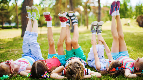 KI generiert: Kinder liegen auf dem Gras und strecken fröhlich die Beine in die Luft.