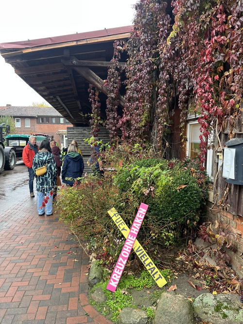KI generiert: Mehrere Leute stehen vor einem Gebäude mit einem Schild: "KREUZ OHNE HAKEN FÜR VIELFALT".
