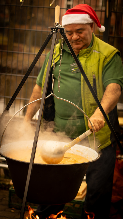 KI generiert: Ein Mann mit Weihnachtsmütze rührt in einem großen Kessel über offenem Feuer.
