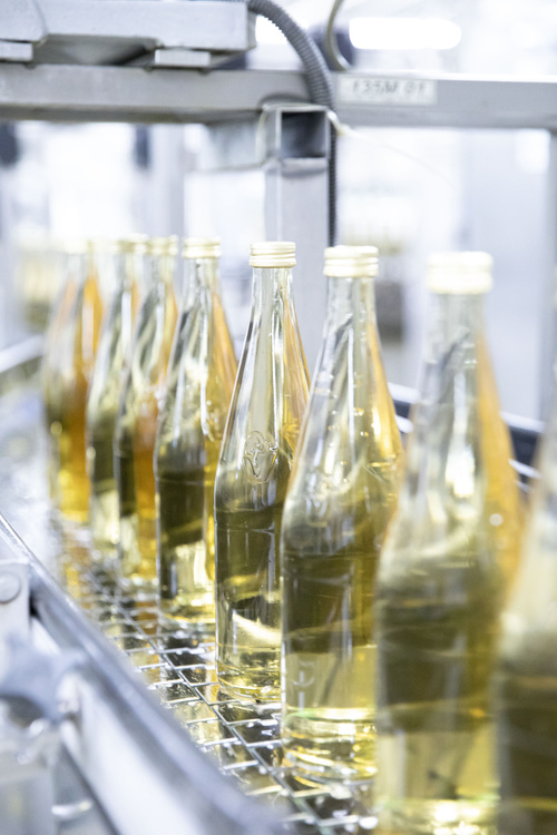 KI generiert: Flaschen mit gelber Flüssigkeit auf einem Förderband in einer Fabrik.