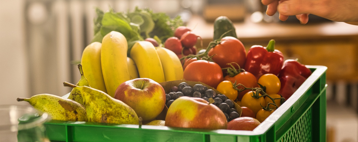 KI generiert: Eine grüne Kiste voller frischem Obst und Gemüse, darunter Bananen und Paprika.