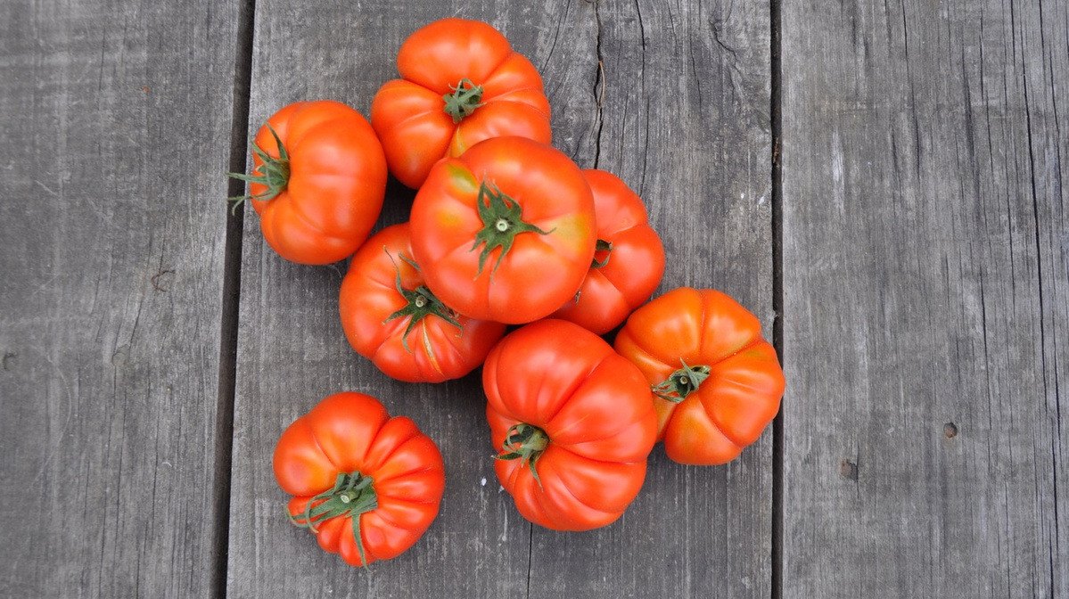 KI generiert: Mehrere rote Tomaten liegen auf einem Holztisch.