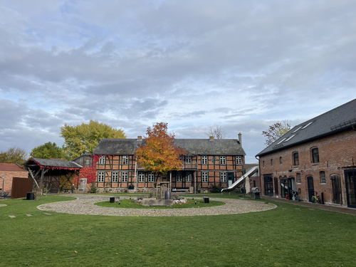 KI generiert: Ein Innenhof mit Rasen, Bäumen und Backsteingebäuden im Hintergrund.