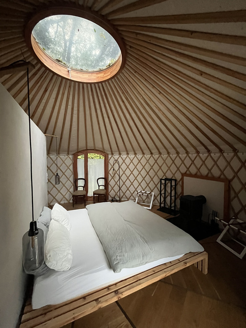 KI generiert: Ein schlicht eingerichtetes Schlafzimmer in einer Jurte mit rundem Dachfenster und Doppelbett.