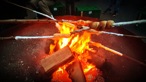 KI generiert: Stockbrot am Lagerfeuer, umgeben von brennendem Holz.
