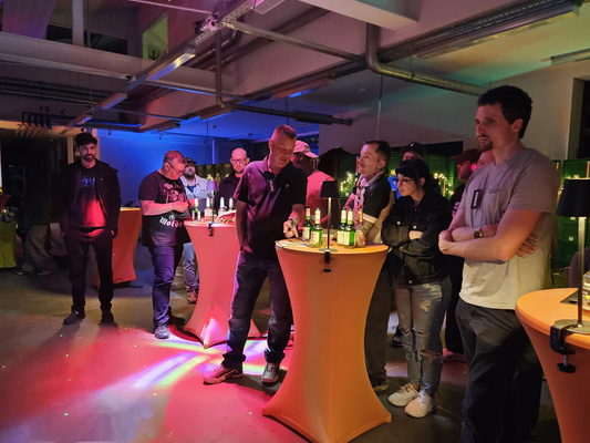 KI generiert: Eine Gruppe von Menschen steht um Stehtische mit Getränken in einem stimmungsvoll beleuchteten Raum.