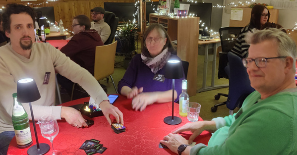 KI generiert: Personen spielen ein Kartenspiel an einem Tisch in einem festlich beleuchteten Raum.