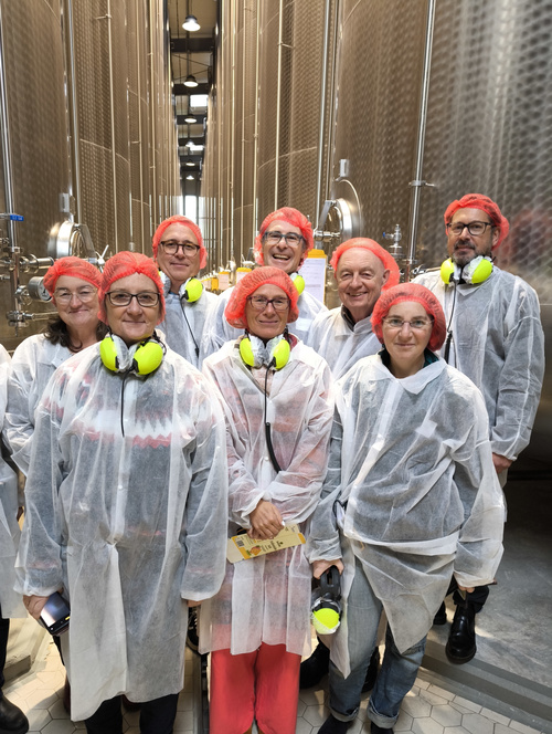 KI generiert: Eine Gruppe von Menschen in Schutzkleidung und roten Haarnetzen steht vor großen Stahltanks.