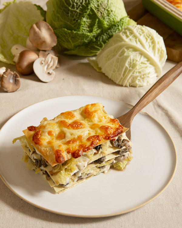 KI generiert: Eine Pilz- und Wirsinglasagne auf einem Teller, daneben frischer Wirsing und Champignons.