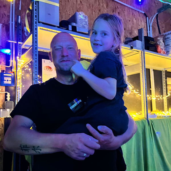 KI generiert: Ein Mann hält ein Kind vor einem Regal mit Lichtern. Auf seinem Shirt steht "CHRISTOPH".