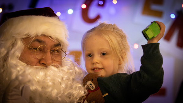 KI generiert: Ein Kind posiert mit dem Weihnachtsmann, das grüne Spielzeug hochhaltend.