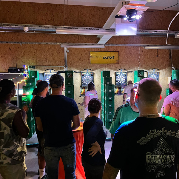 KI generiert: Menschen spielen Darts in einer Halle. Ein Schild zeigt "Piotre Karotte dartort".