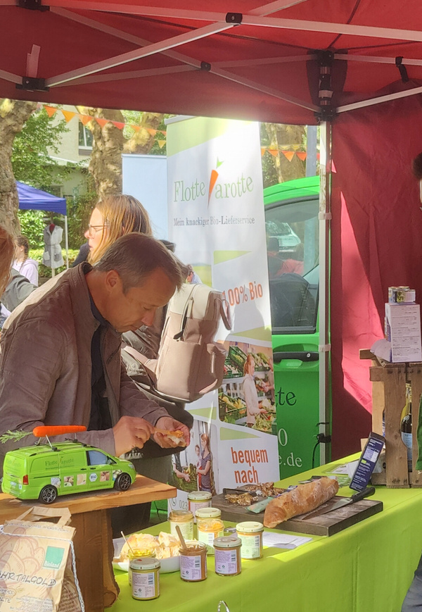 KI generiert: Ein Mann probiert Brot an einem Bio-Stand mit dem Banner "Flotte Karotte".
