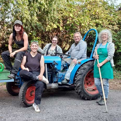 KI generiert: Eine Gruppe von fünf Personen posiert um einen alten blauen Traktor.